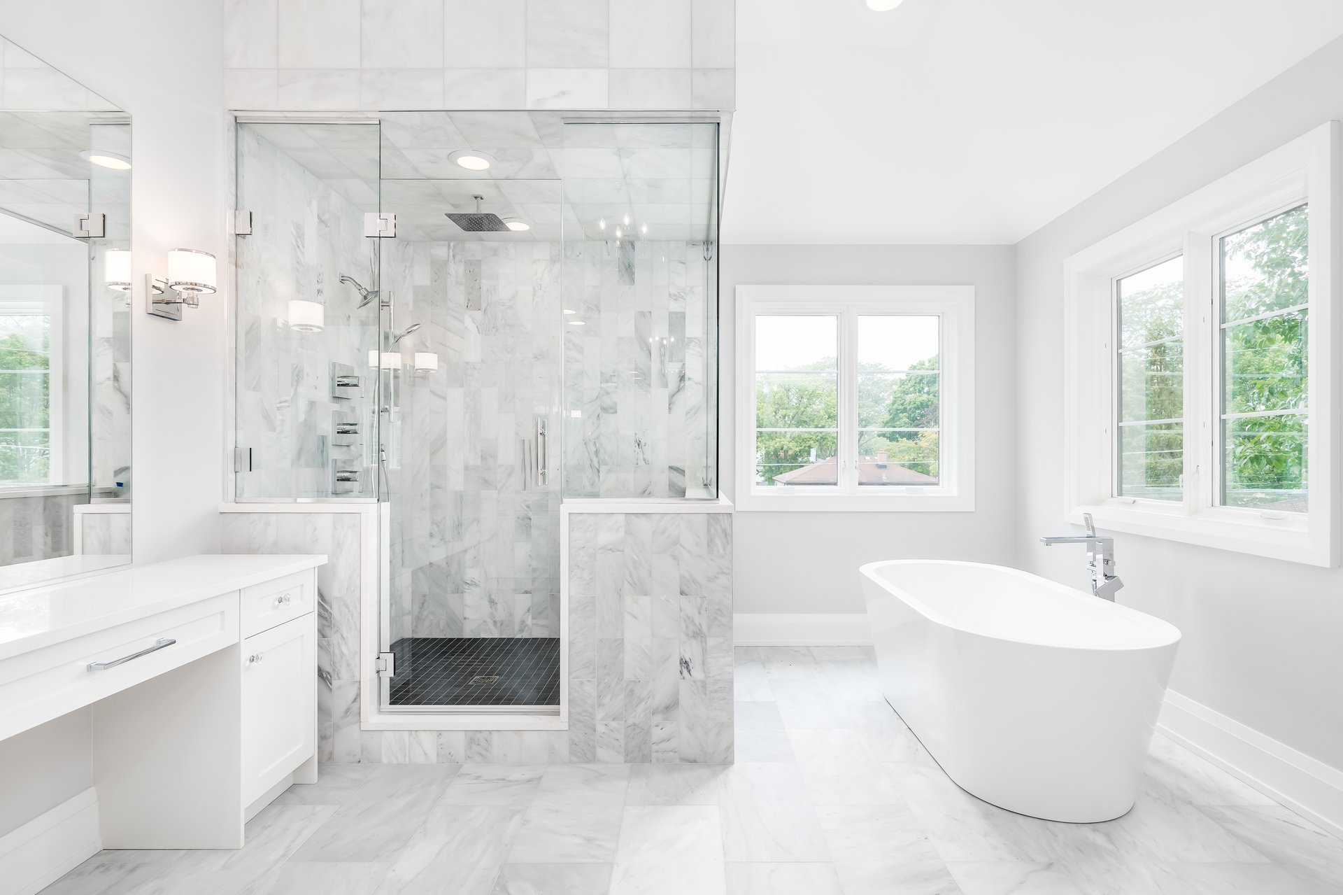 A large luxurious bathroom with a stand alone tub, white vanity, and a glass stand up shower with marble tiles