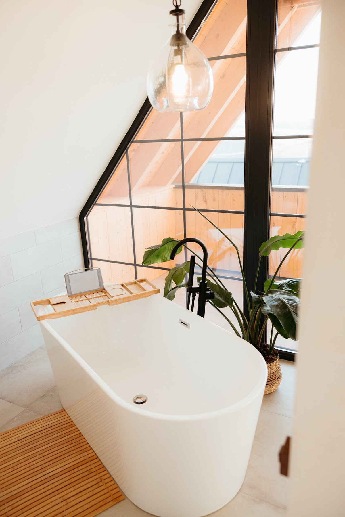 Modern bathroom featuring a freestanding bathtub positioned beneath a triangular window, creating a bright and airy ambiance
