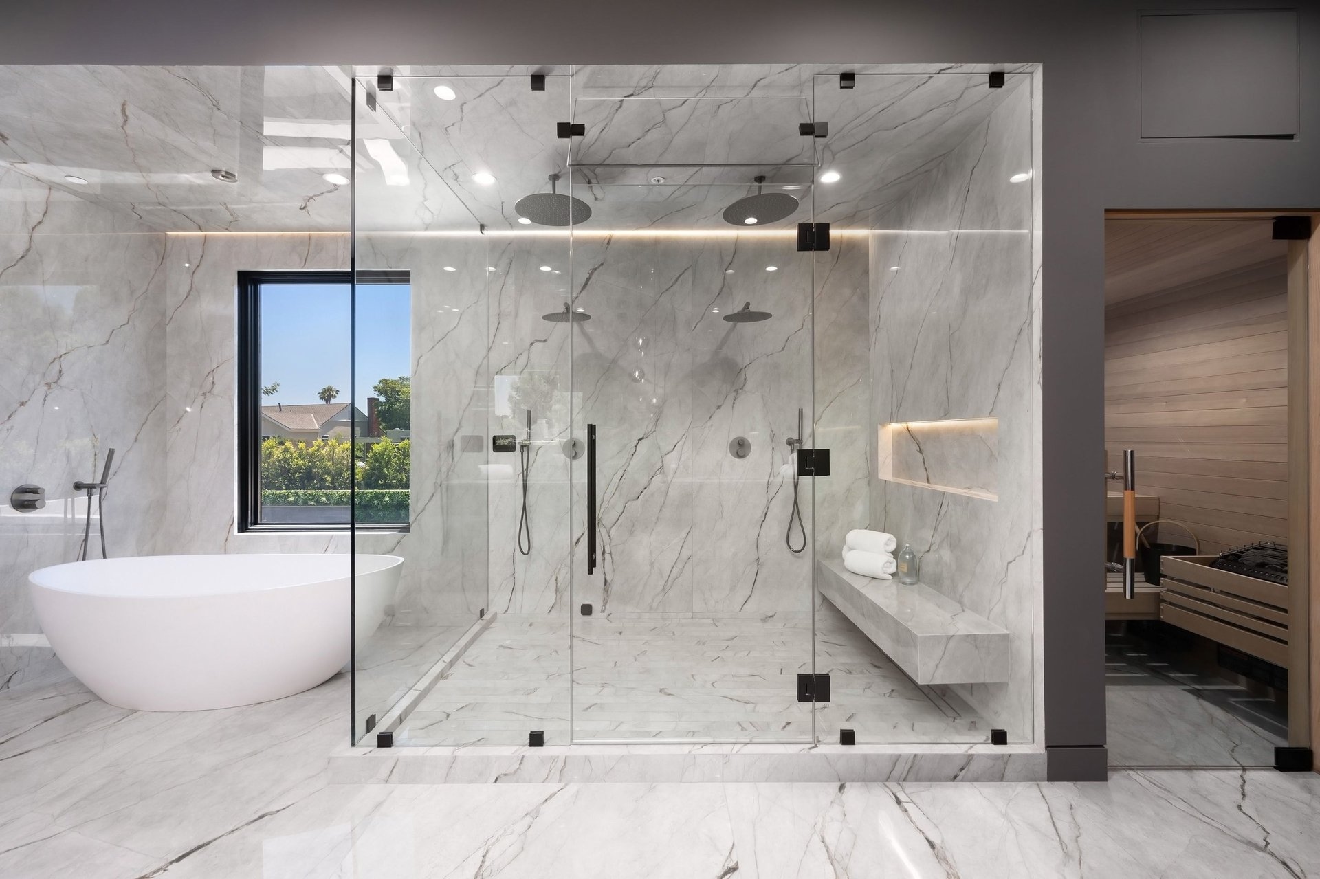 Modern luxury bathroom with a large glass shower, freestanding tub, and sauna, featuring marble walls and floors
