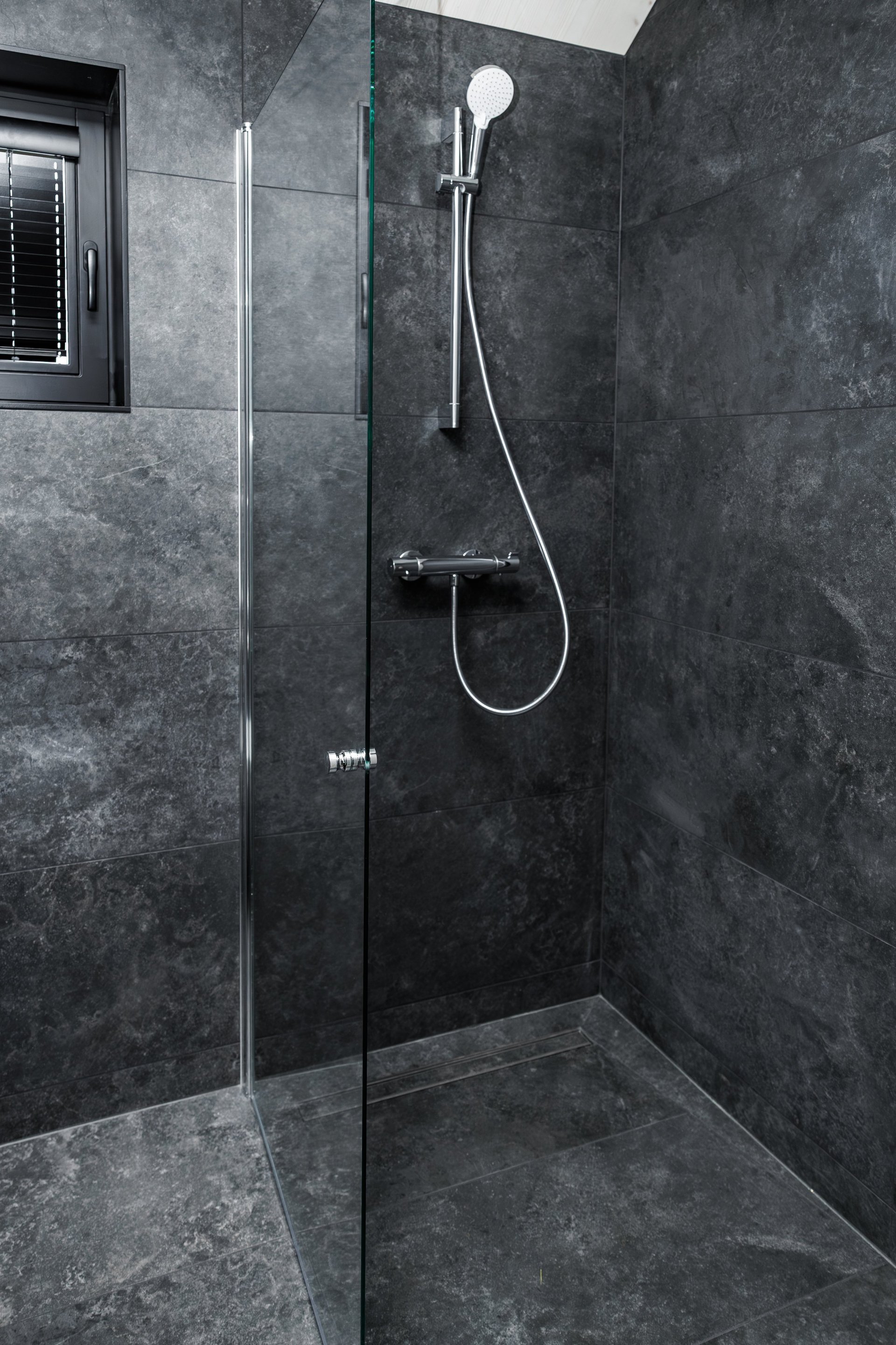 Modern walk-in shower with dark grey tiles and chrome fixtures