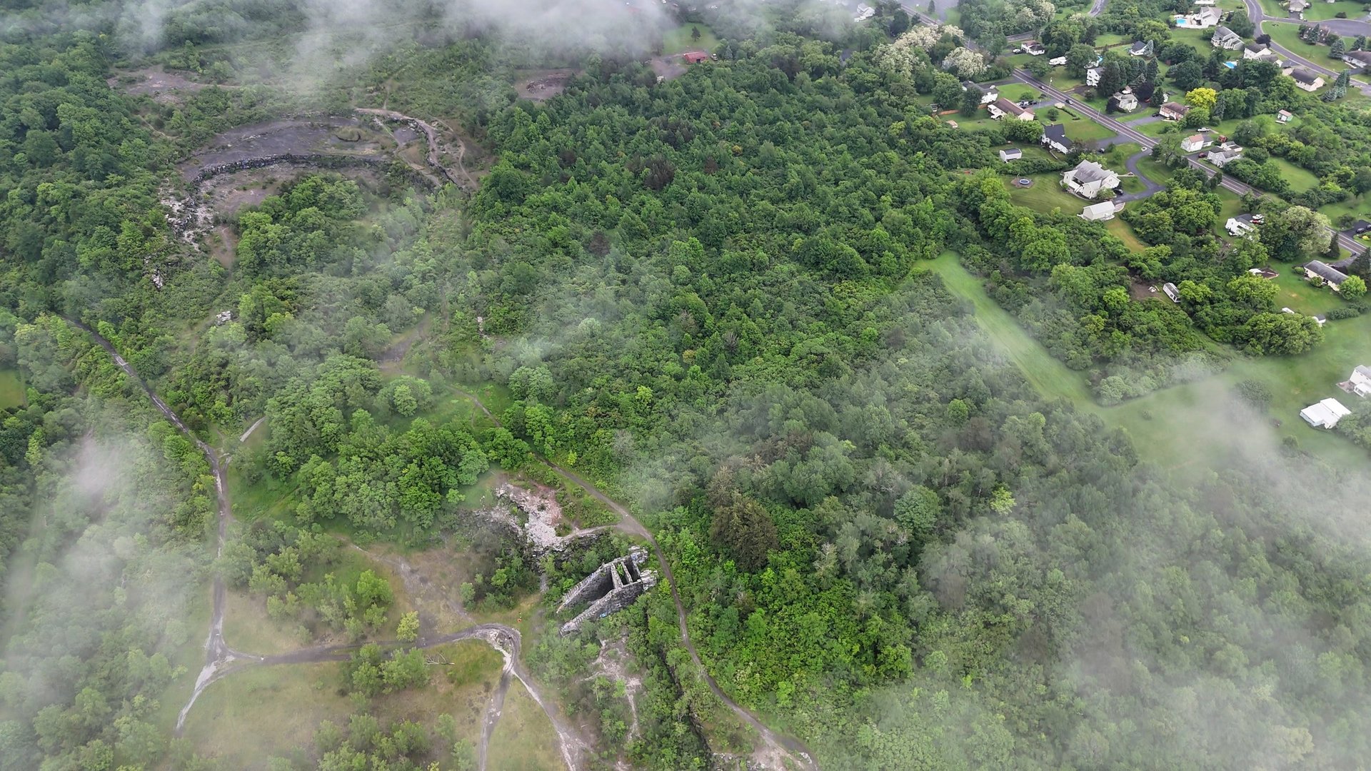 Clouds slowly pass between the view of a large stretch of real estate covered by forest and a site that holds the remnants of a vacant quarry as well as the location that was used to produce munitions at one point in time.